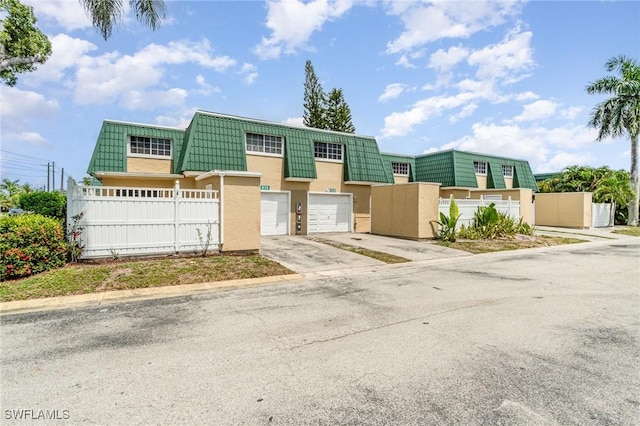 5816 Whiting Ct, Fort Myers, FL 33919 - townhome / multi-family property featuring stucco siding, concrete driveway, a fenced front yard, a garage, and mansard roof