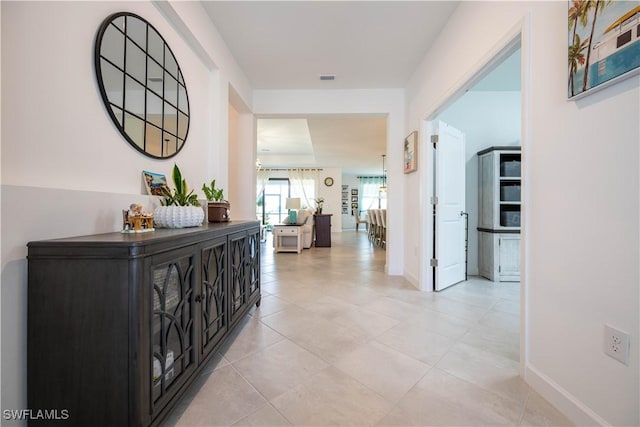 hall with visible vents, baseboards, and light tile patterned flooring