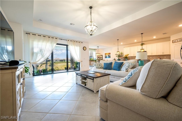 living room featuring a tray ceiling, a chandelier, light tile patterned flooring, and visible vents