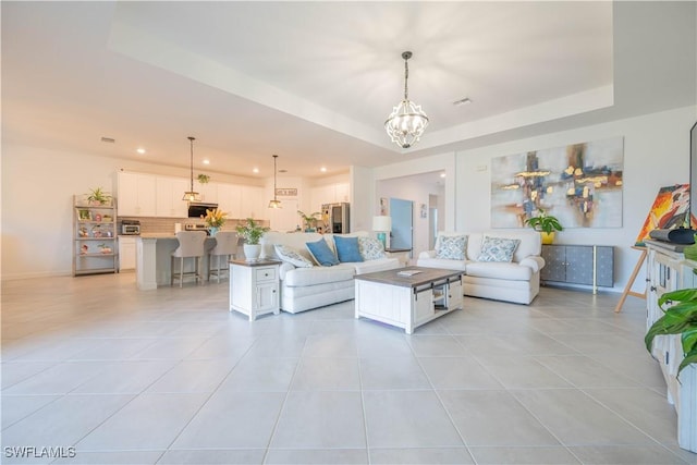 living area featuring a tray ceiling, baseboards, a chandelier, and light tile patterned flooring