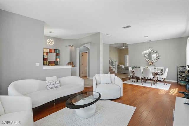 living room with arched walkways, stairway, wood finished floors, and baseboards