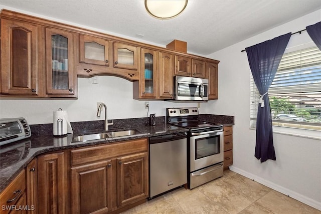 kitchen featuring glass insert cabinets, baseboards, a sink, dark stone countertops, and appliances with stainless steel finishes