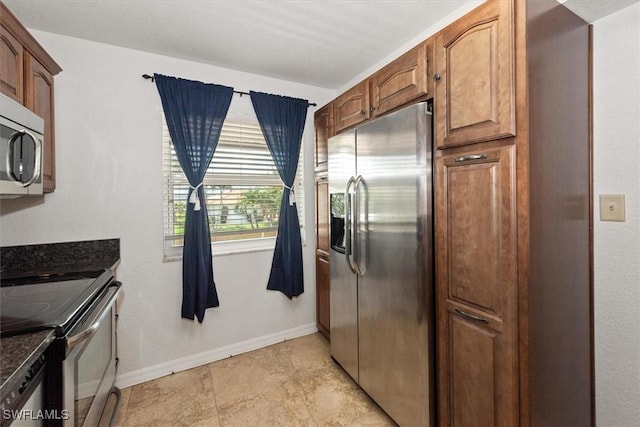 kitchen featuring appliances with stainless steel finishes, brown cabinetry, baseboards, and dark stone countertops