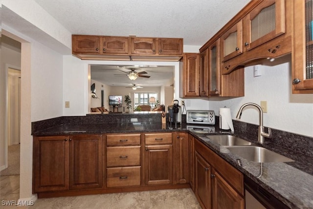 kitchen with dark stone counters, glass insert cabinets, a ceiling fan, and a sink