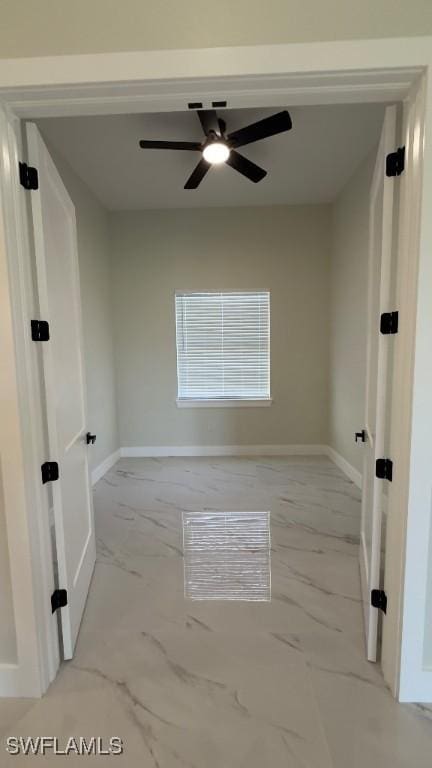 empty room featuring a ceiling fan, marble finish floor, and baseboards