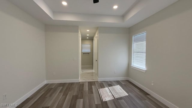 empty room with baseboards, a tray ceiling, recessed lighting, and wood finished floors