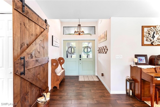 entrance foyer featuring dark wood-style flooring, a barn door, baseboards, and a notable chandelier