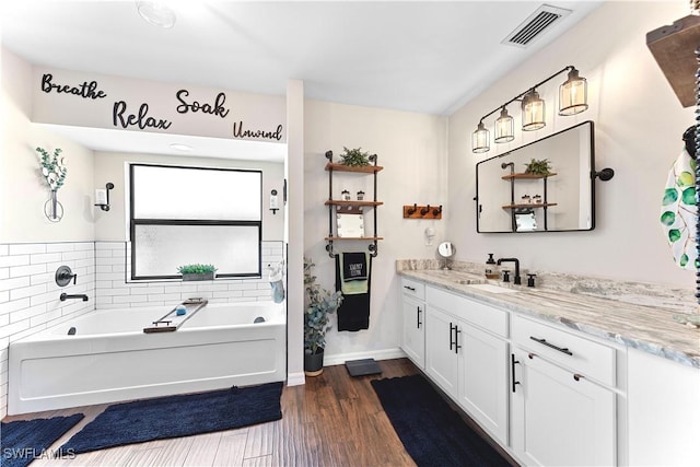 full bath featuring vanity, a garden tub, visible vents, and wood finished floors