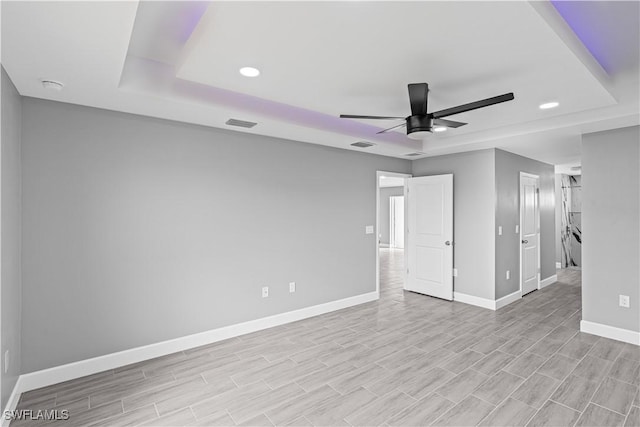 interior space featuring a tray ceiling, baseboards, light wood-type flooring, and recessed lighting