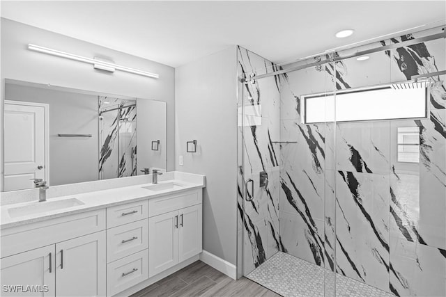 full bath featuring a marble finish shower, double vanity, a sink, and wood finished floors