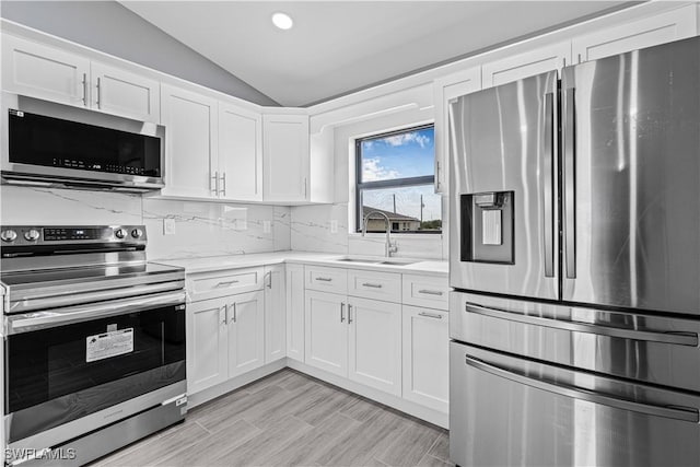 kitchen with recessed lighting, a sink, white cabinetry, vaulted ceiling, and appliances with stainless steel finishes