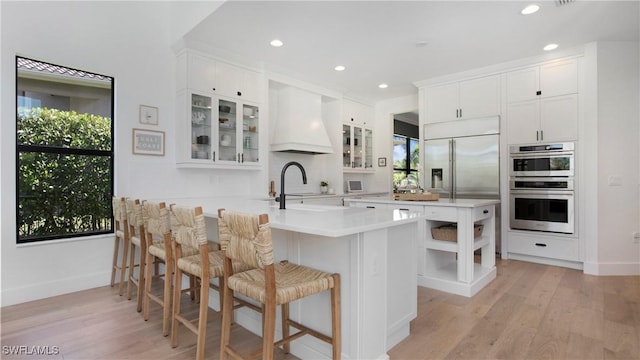 2954 Cinnamon Bay Cir, Naples, FL 34119 - kitchen featuring custom exhaust hood, a kitchen breakfast bar, stainless steel double oven, light countertops, and light wood-style floors