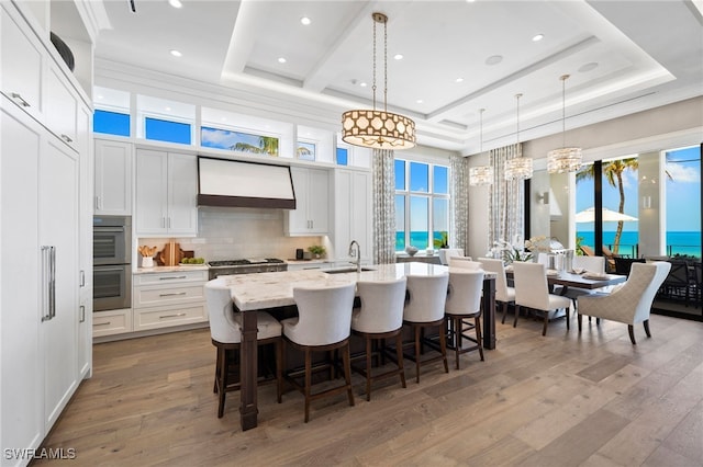 26924 Hickory Blvd, Bonita Springs, FL 34134 - kitchen featuring premium range hood, light wood-style floors, a kitchen breakfast bar, white cabinetry, and an island with sink