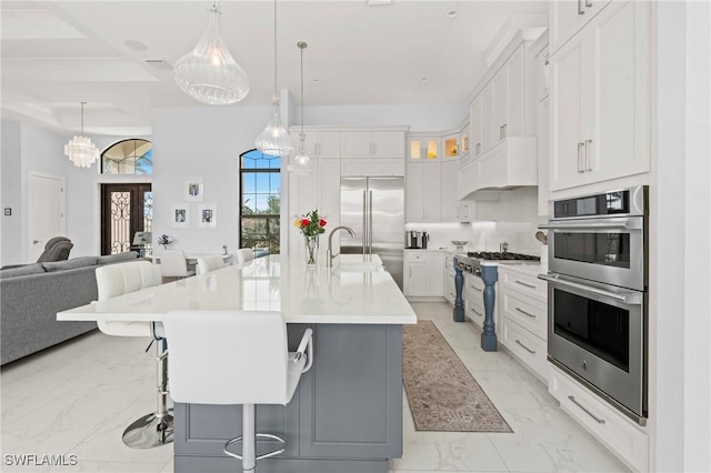 388 Pine Ave, Naples, FL 34108 - kitchen with stainless steel appliances, light marble finish floors, white cabinetry, open floor plan, and a breakfast bar