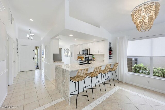 kitchen with appliances with stainless steel finishes, a chandelier, light tile patterned flooring, a peninsula, and vaulted ceiling