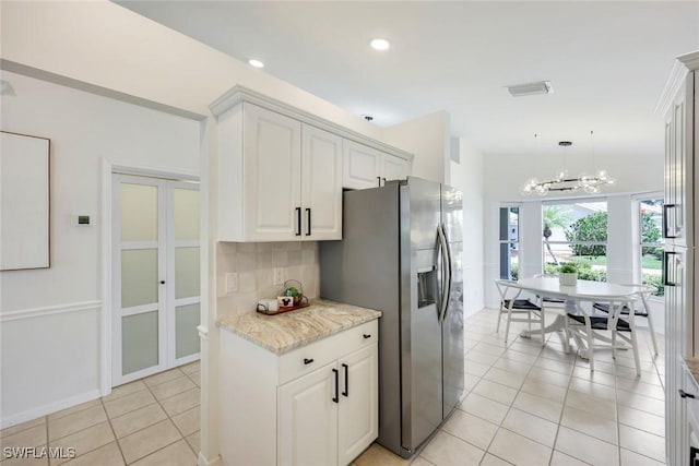 kitchen featuring stainless steel refrigerator with ice dispenser, a chandelier, tasteful backsplash, light tile patterned floors, and white cabinets