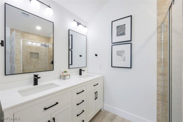 bathroom with a shower stall, double vanity, wood finished floors, and baseboards
