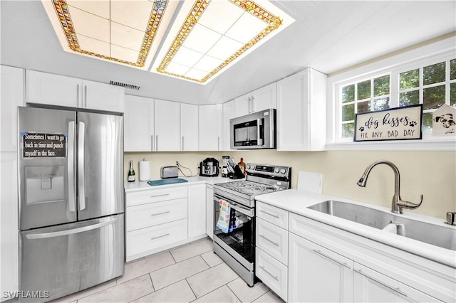 kitchen with appliances with stainless steel finishes, light tile patterned flooring, light countertops, and white cabinetry