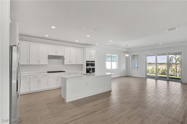 kitchen with under cabinet range hood, open floor plan, black stovetop, white cabinetry, and recessed lighting