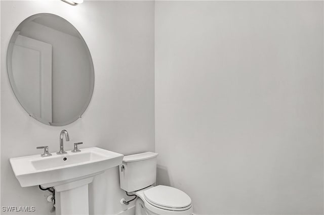 half bath featuring toilet, baseboards, and a sink