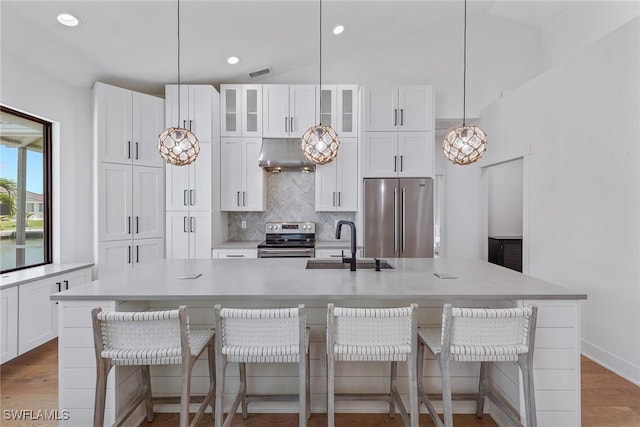 kitchen with stainless steel appliances, a sink, under cabinet range hood, backsplash, and white cabinets