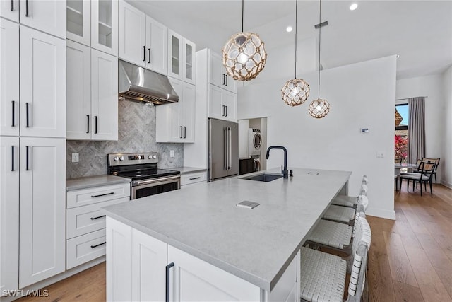 kitchen with appliances with stainless steel finishes, under cabinet range hood, a sink, a center island with sink, and tasteful backsplash