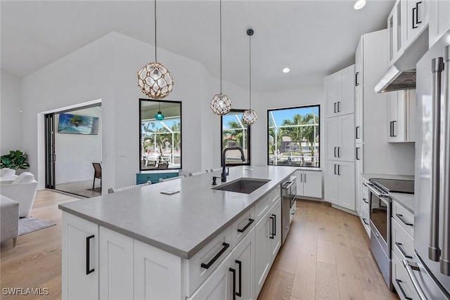 kitchen featuring a sink, stainless steel appliances, light wood-style flooring, a center island with sink, and decorative light fixtures