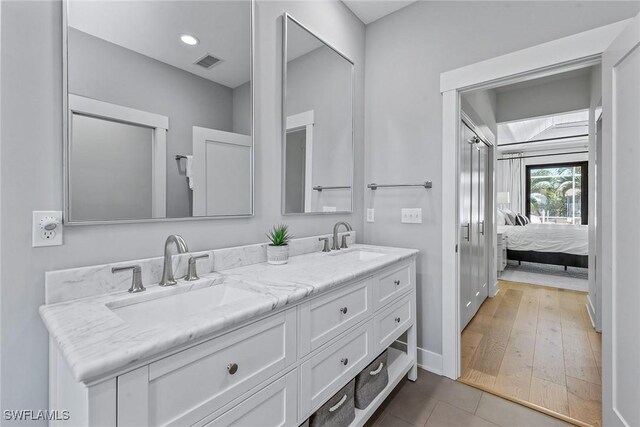 ensuite bathroom featuring double vanity, tile patterned floors, and baseboards