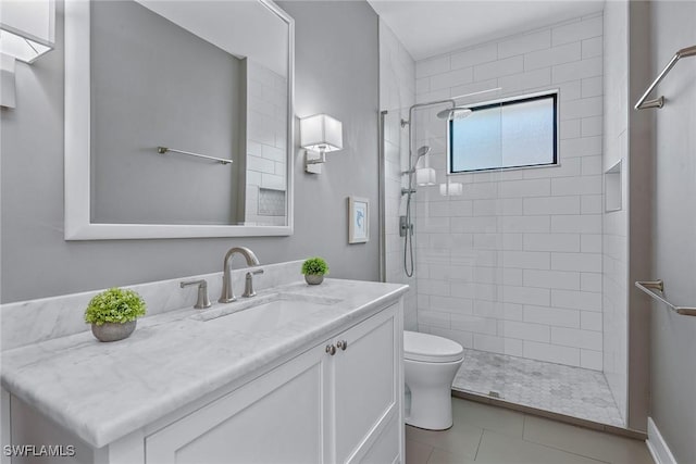 bathroom with toilet, tiled shower, vanity, and tile patterned floors