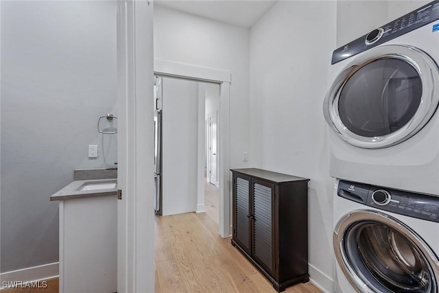 washroom with stacked washer / dryer, light wood finished floors, and baseboards