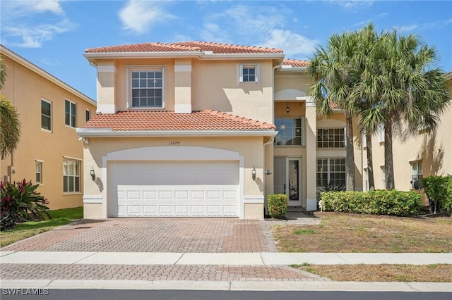 mediterranean / spanish house featuring a tiled roof, an attached garage, driveway, and stucco siding