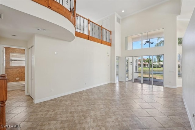 unfurnished living room with a towering ceiling, ceiling fan, plenty of natural light, and tile patterned floors