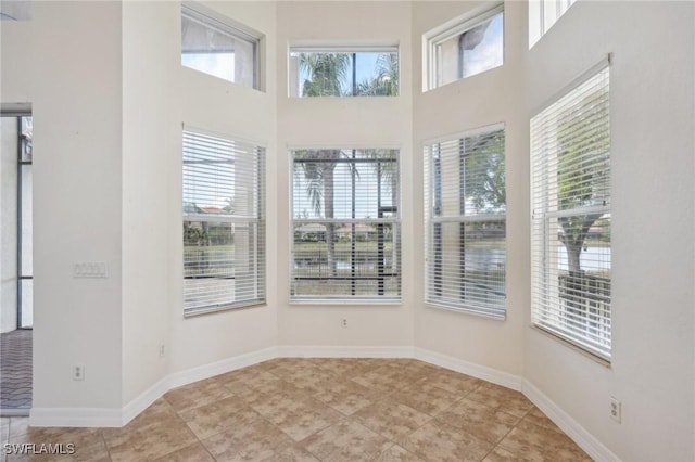 spare room featuring light tile patterned floors, baseboards, and a towering ceiling