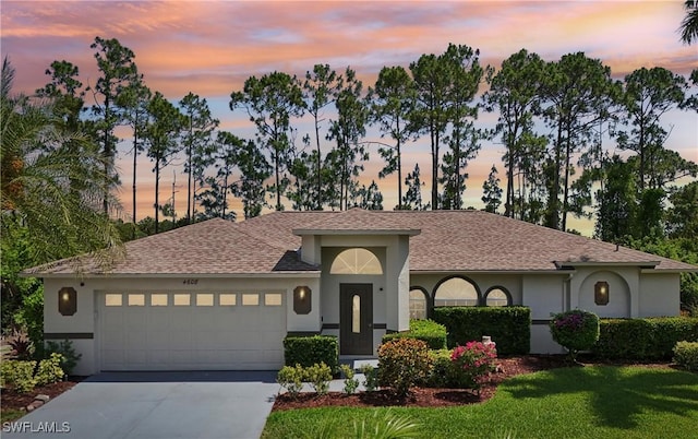 mediterranean / spanish-style home featuring an attached garage, stucco siding, concrete driveway, a shingled roof, and a lawn