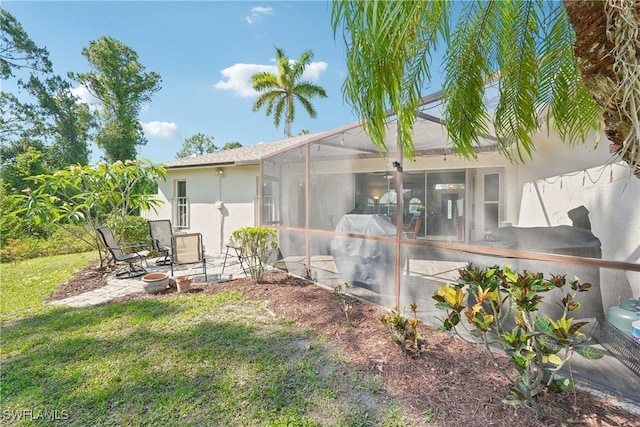 back of house with stucco siding, a patio, a yard, and a lanai