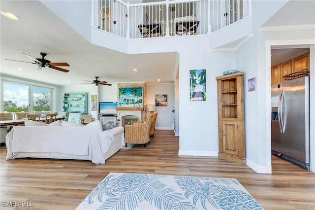living area with baseboards, a ceiling fan, a high ceiling, light wood-style floors, and recessed lighting