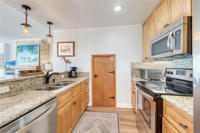 kitchen featuring appliances with stainless steel finishes, a sink, light wood finished floors, and light stone countertops