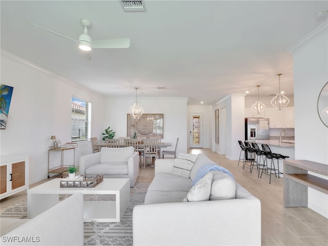 living area with a chandelier, ceiling fan, crown molding, light wood finished floors, and baseboards