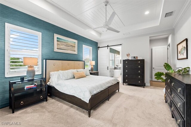 bedroom featuring light colored carpet, a tray ceiling, a barn door, baseboards, and ensuite bath