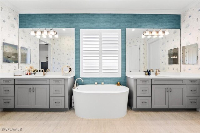 full bath with wallpapered walls, crown molding, a freestanding tub, and two vanities