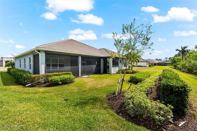 back of house with a sunroom, a yard, a tile roof, and stucco siding