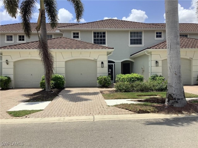 view of front of home featuring a tile roof, an attached garage, stucco siding, and decorative driveway