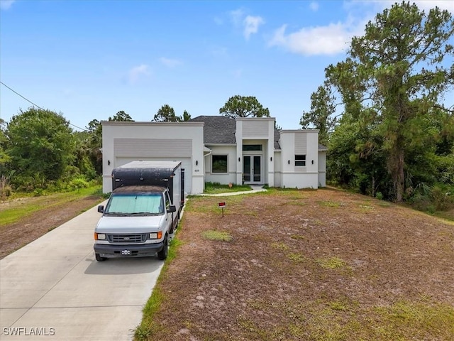 409 Columbus Blvd S, Lehigh Acres, FL 33974 - modern home with driveway, french doors, stucco siding, an attached garage, and roof with shingles
