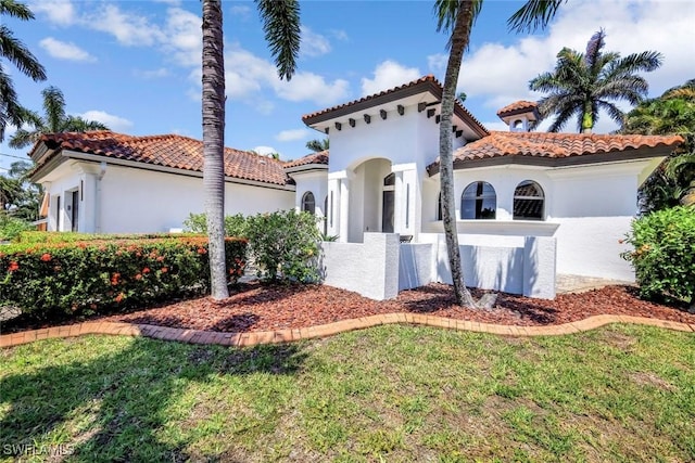 mediterranean / spanish house with stucco siding, a tiled roof, and a front lawn