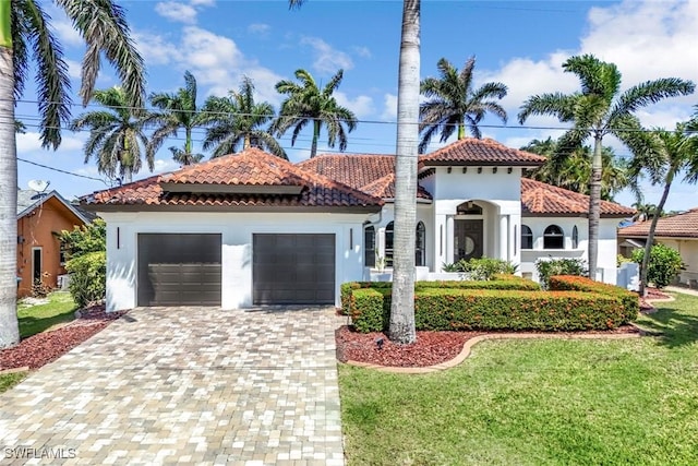 mediterranean / spanish house with a tile roof, decorative driveway, an attached garage, stucco siding, and a front lawn