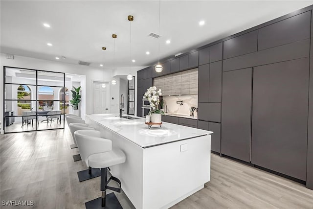 kitchen with a sink, light wood-style flooring, a center island with sink, recessed lighting, and light countertops