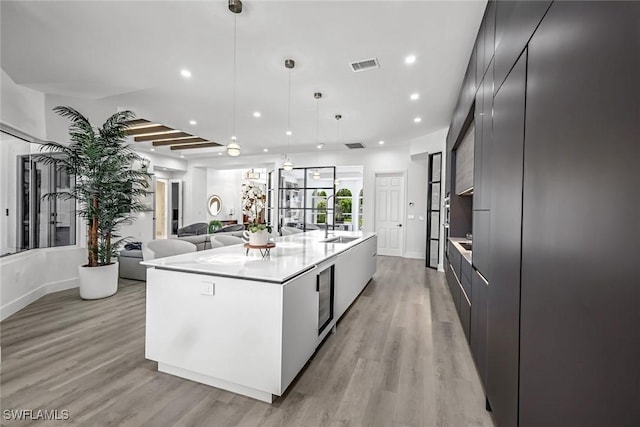 kitchen with modern cabinets, light wood-type flooring, a sink, light countertops, and a spacious island
