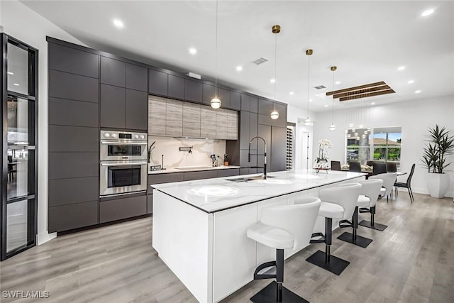 kitchen with modern cabinets, a sink, double oven, light wood-style floors, and recessed lighting