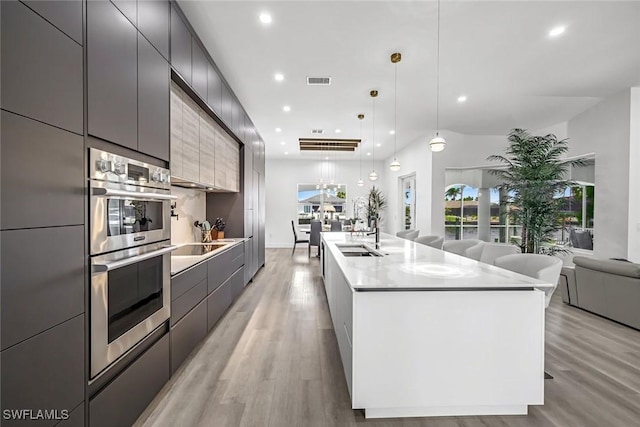 kitchen with modern cabinets, double oven, a sink, light wood finished floors, and recessed lighting