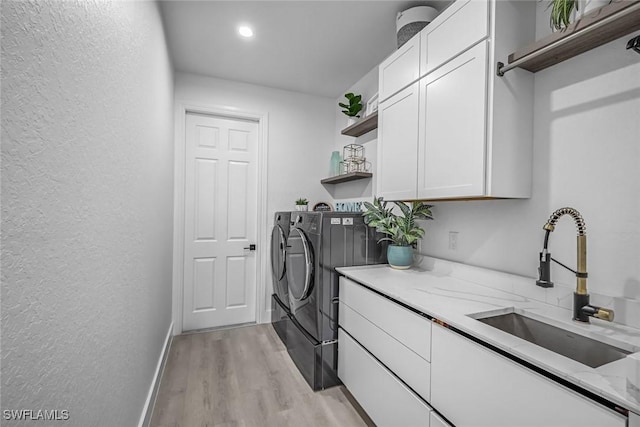 washroom with independent washer and dryer, cabinet space, light wood-style flooring, a textured wall, and baseboards